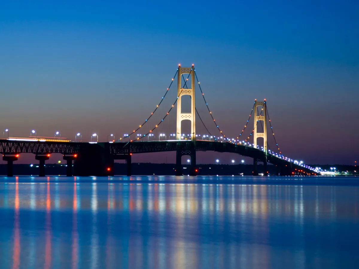 The Mackinac Bridge lit at dusk, reflected in the Straits