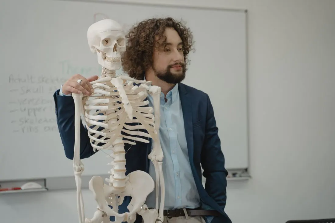 A biology teacher beside a skeleton model