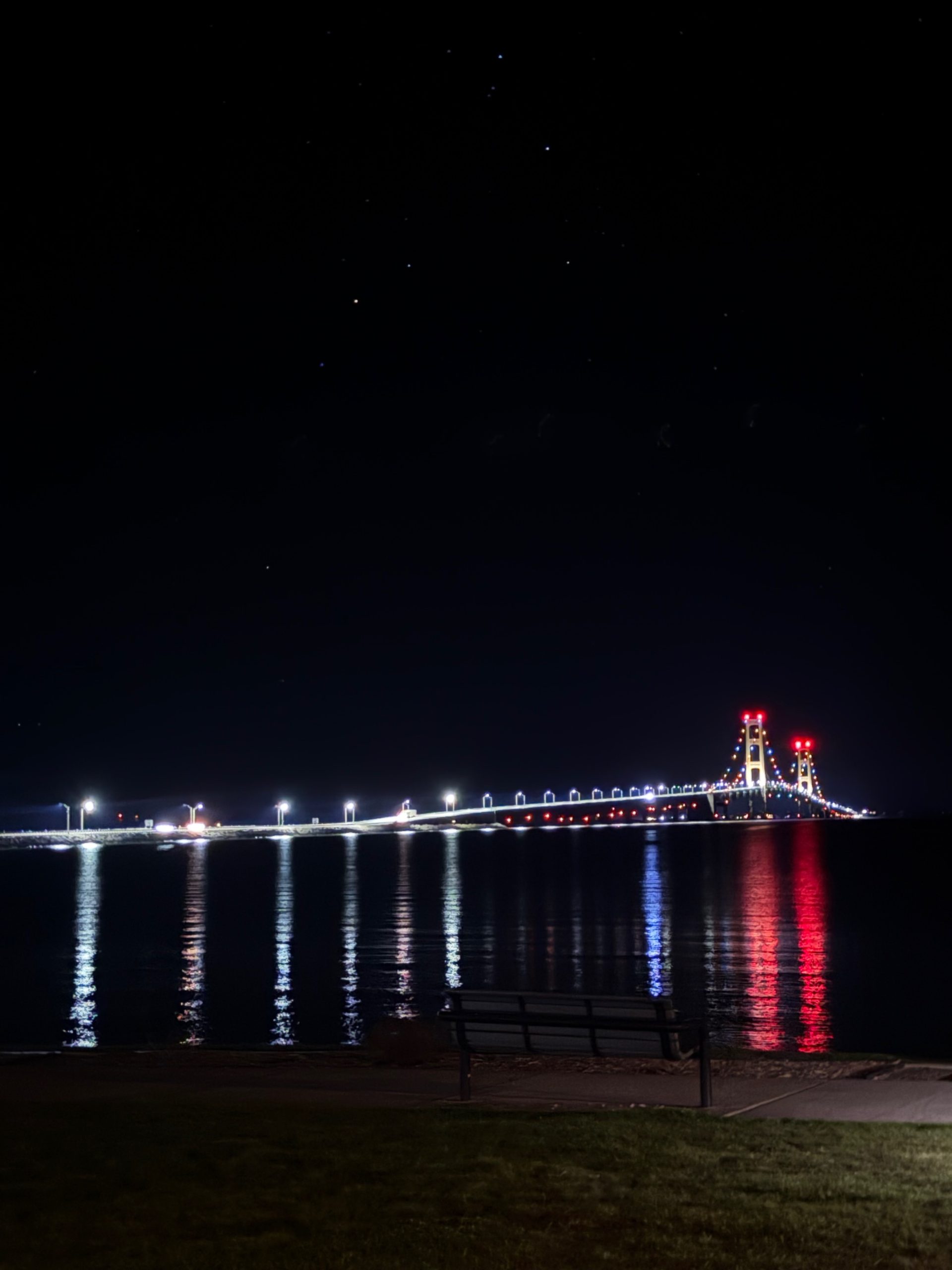 The Mackinac Bridge lit at night, reflected in the Straits of Mackinac