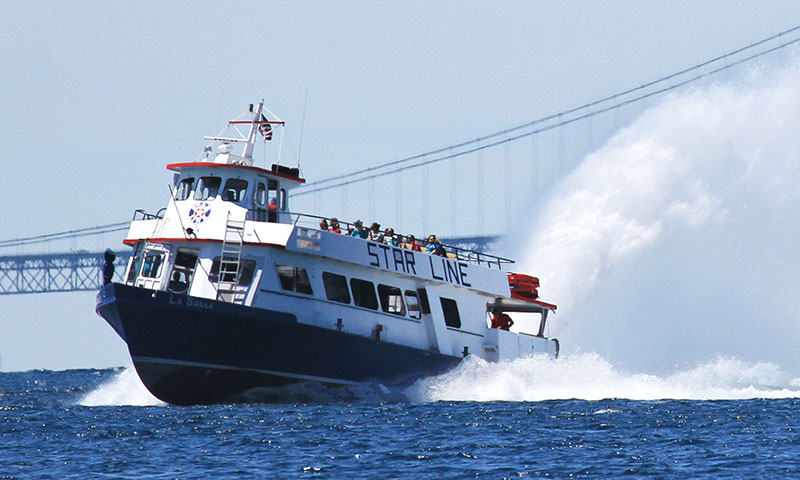 A Star Line hydro-jet ferry throwing a rooster tail beneath the Mackinac Bridge